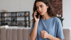 Mladá žena telefonuje doma a vyzerá vážne. Hovor cez mobil v obývačke.