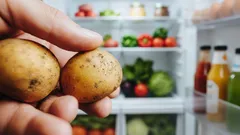Čerstvé zemiaky v ruke pred otvorenou chladničkou plnou zeleniny a ovocia