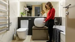 Moderná kúpeľňa s umývadlom, WC a ženou pri zrkadle, interiér v štýle minimalizmu.