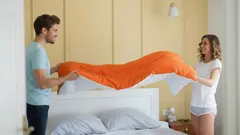 Mladý pár ustieľa posteľ s oranžovou prikrývkou v modernej spálni.