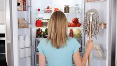 Žena s mopom čistí chladničku plnú potravín, pohľad zozadu, domáce upratovanie