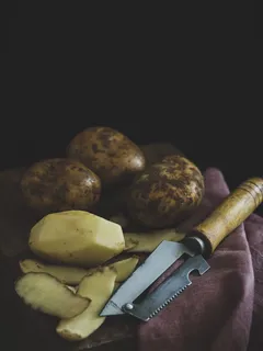 Ošúpané a neošúpané zemiaky na drevenom stole s jasnou žltou farbou