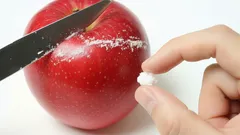 Červené jablko, nôž a ruka s bielou tabletkou, koncept zdravia a vitamínov.